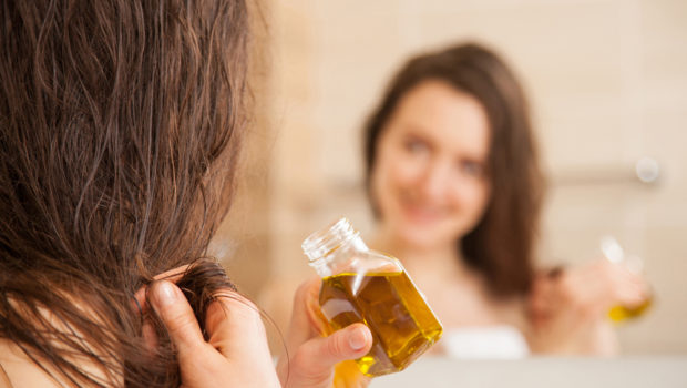 smiling-young-woman-applying-oil-mask-to-hair-tips-in-front-of-a-mirror-haircare-concept-390196507.jpg